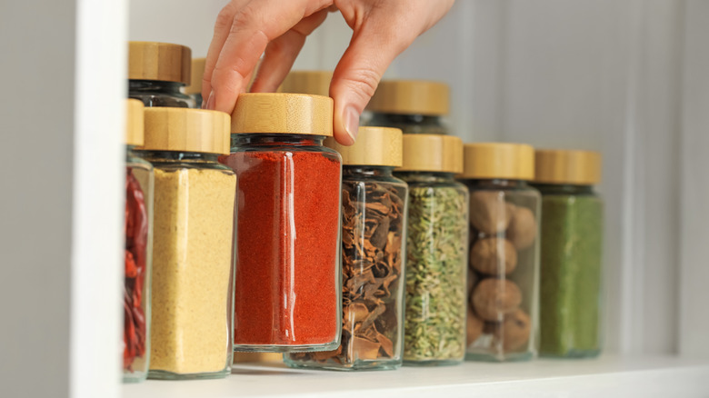 Person reaching for a jar of spices from a cabinet