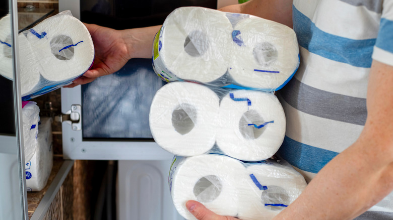 A man stores toilet paper in a cluttered cabinet
