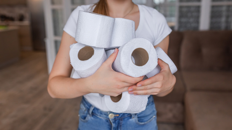 a woman carries several loose toilet paper rolls