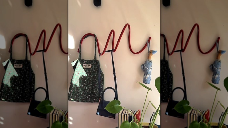 A red curvy DIY coat rack with bags hanging from it and a cart of books and plants beneath.