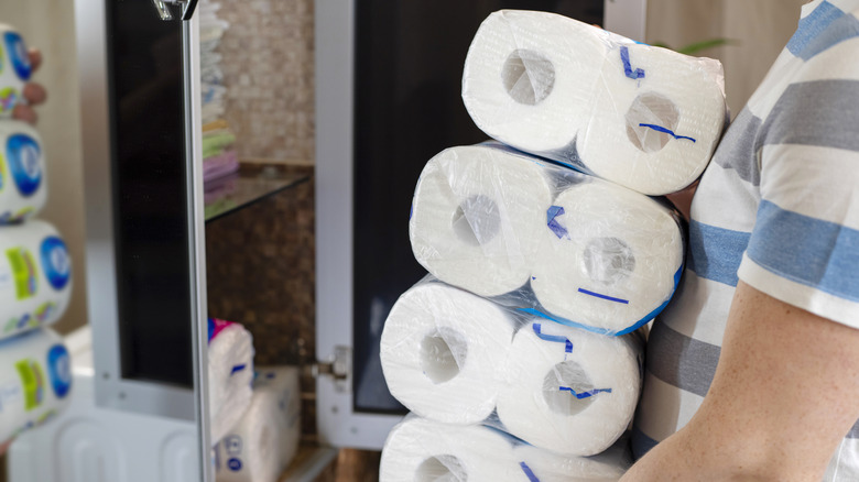 Person carrying a stack of toilet paper packages