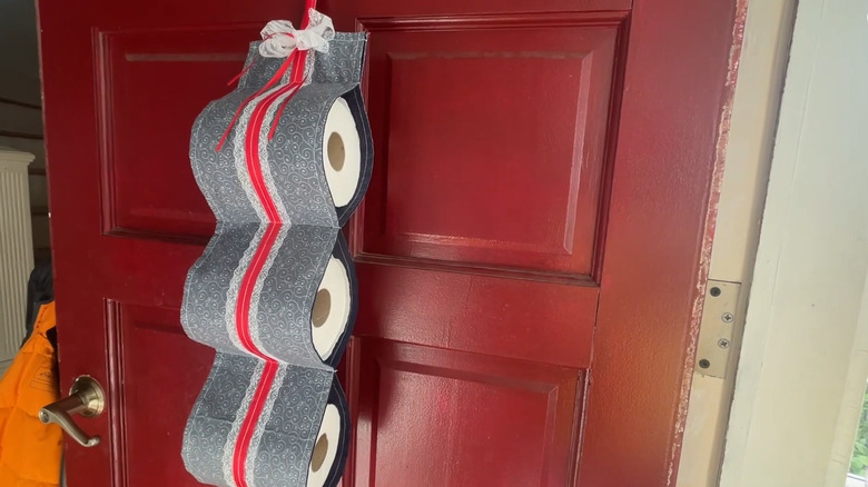 DIY fabric toilet paper holder with three rolls of toilet paper in it hanging on a door