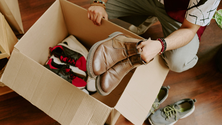 A man placing a pair of brown boots into a box containing other shoes.
