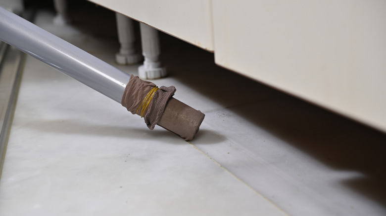 Pantyhose tightened around the hose of a vacuum cleaner sweeping under furniture