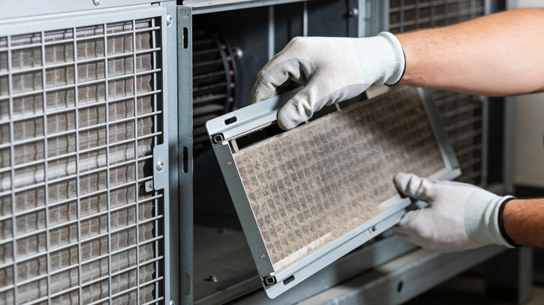 A person in protective gloves is carefully taking out a clogged air filter from a large ventilation system