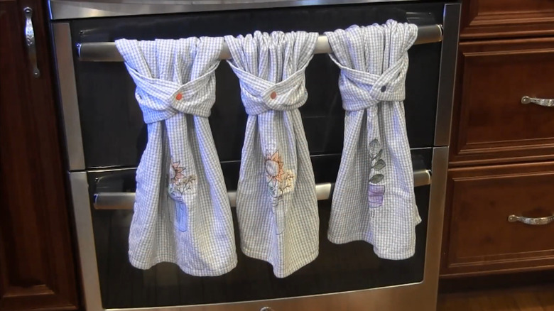 Three gingham towels hanging on a stove handle with snaps holding them in place