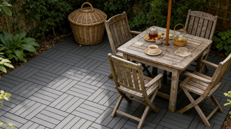 Gray composite pavers form a grid under an outdoor dining set, surrounded by vegetation.