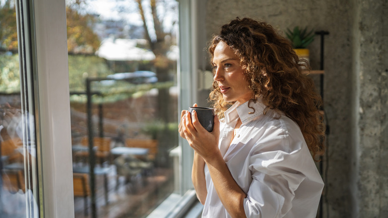 A woman looking out of a window holding a mug of coffee