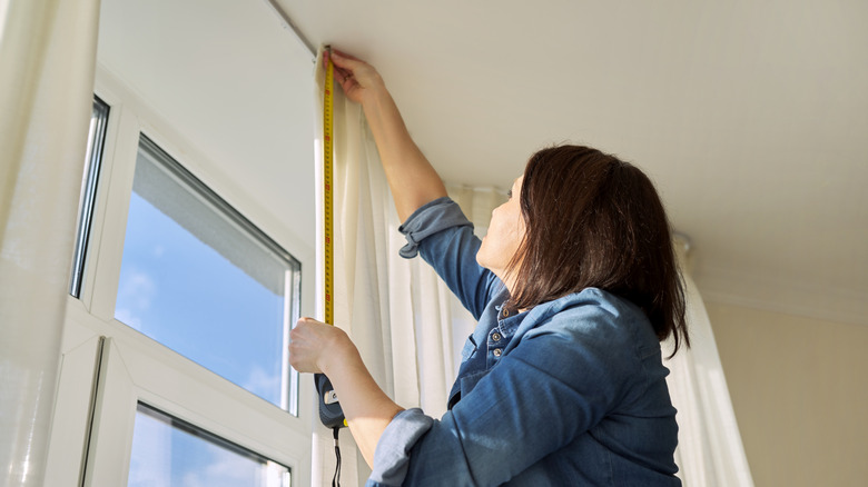 A woman measuring a window with a tape measure