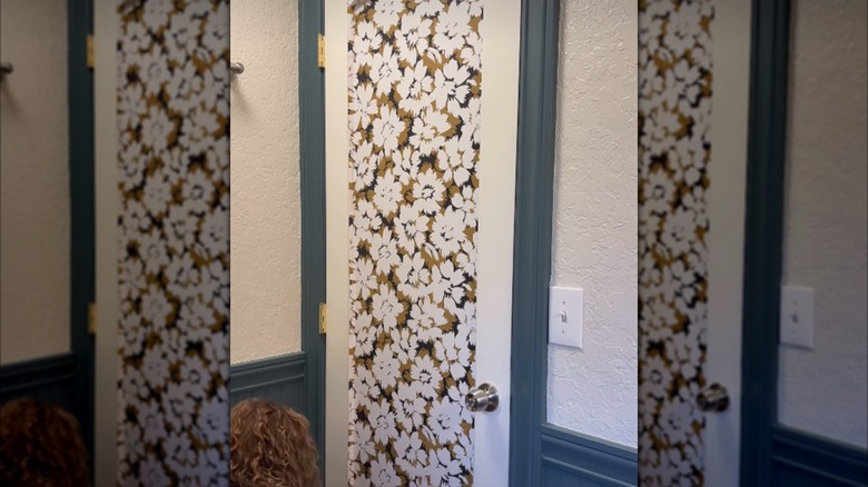 Woman applying patterned wallpaper over a glass panel in a door