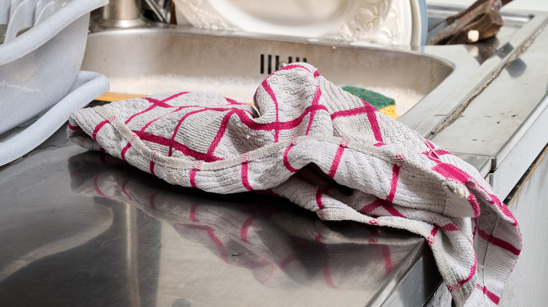 A dirty white and red checkered dish towel laying beside sink