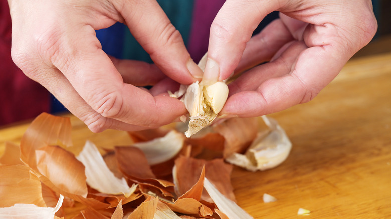Person peeling garlic over pile of garlic and onion peels
