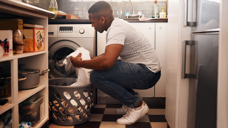 A man crouches while filling a washing machine