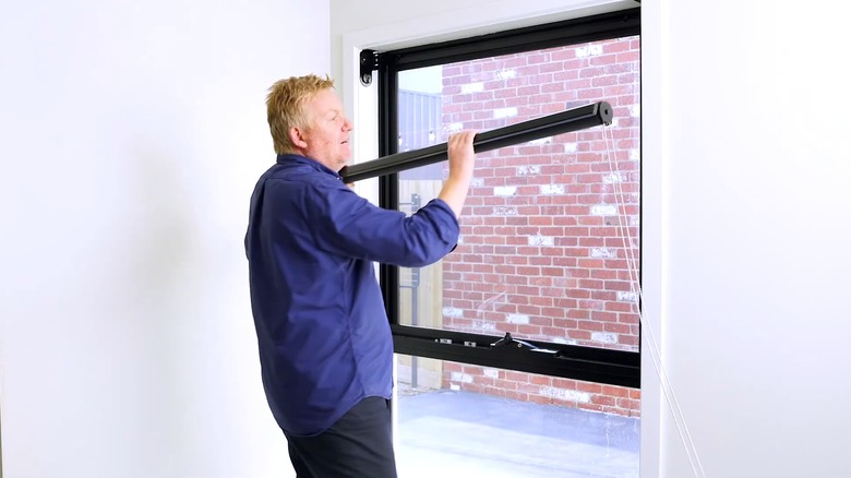 Man installing the bottom layer of a double roller blind over a window