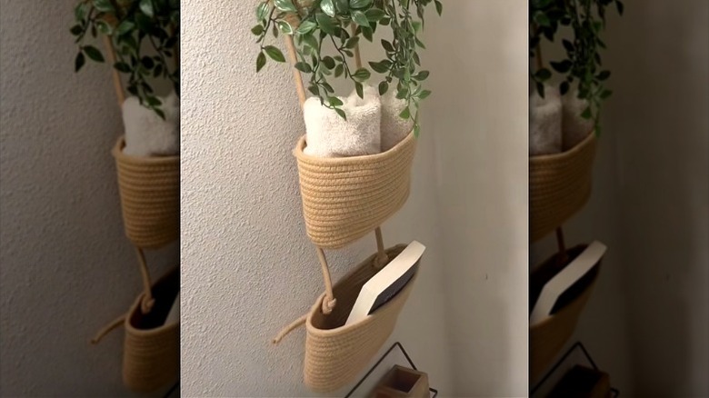 A three-tier woven hanging fruit basket in the bathroom with toiletries and a plant above the toilet