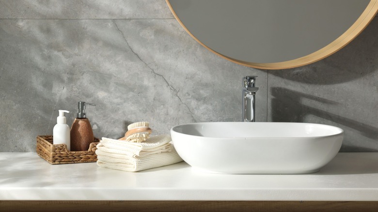 A modern bathroom countertop with a sink, towels, and toiletries