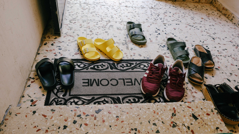 A bunch of colorful shoes by a welcome mat