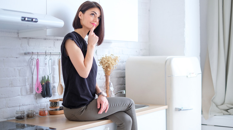 A woman sits on her kitchen countertop, thinking