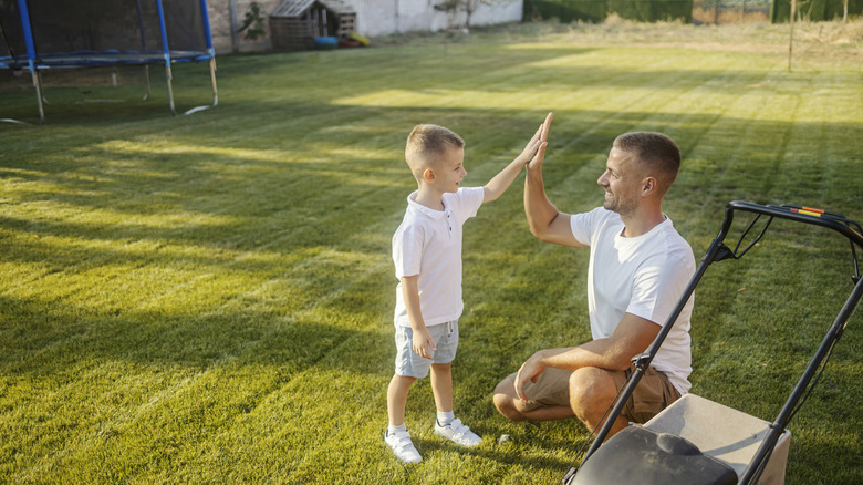 Father and son high-fiving after mowing a perfectly level lawn.