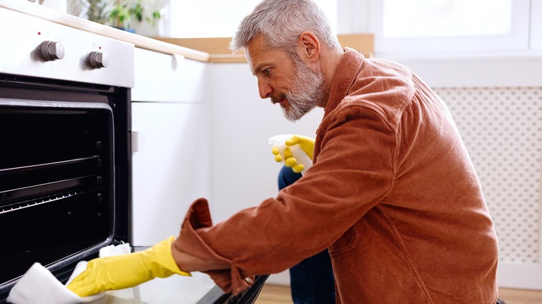 Man cleaning oven with spray bottle and paper towels