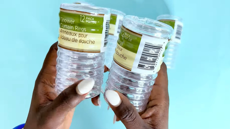 Person holding two packages of clear Dollar Tree plastic shower rings