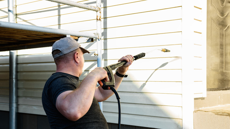 Man using a pressure washer to clean a vinyl siding