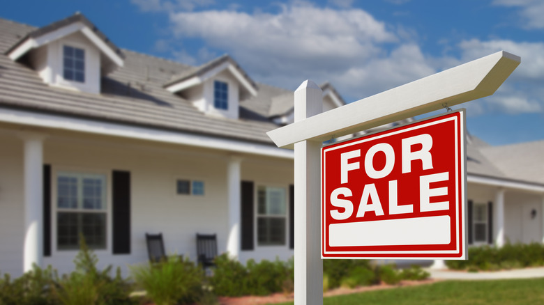 for sale sign in the yard of a nice home in the background