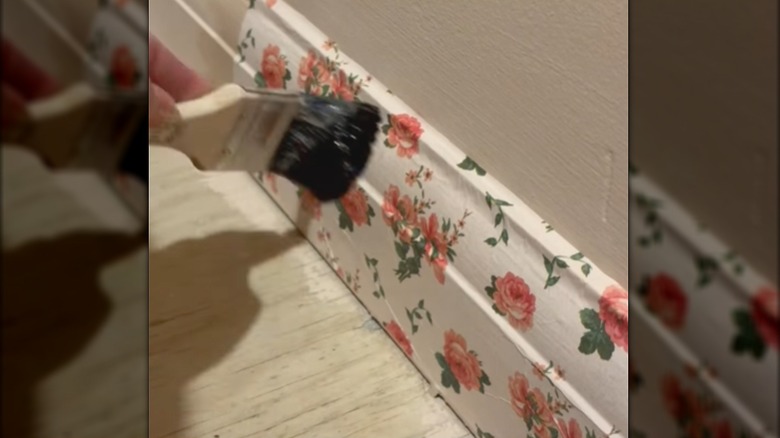Person brushing glue over floral tissue paper being decoupaged onto the baseboards