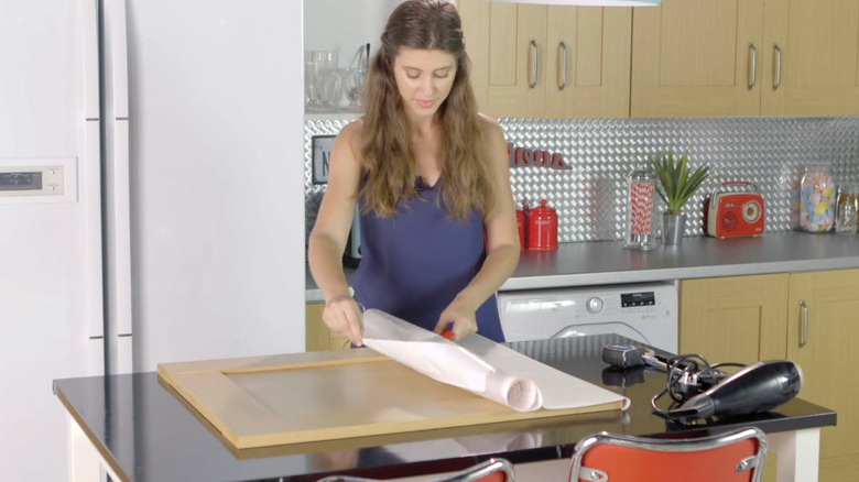 Person applying white vinyl wrap to a kitchen cabinet door