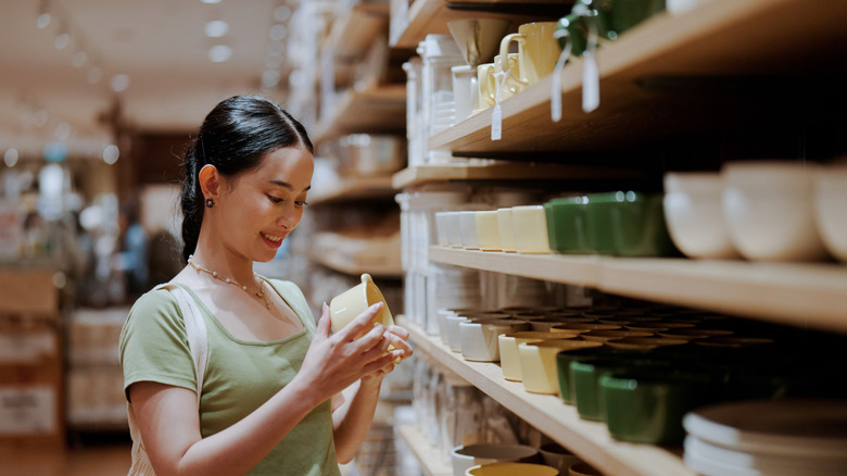 A woman looking at dishware at a thrift shop.