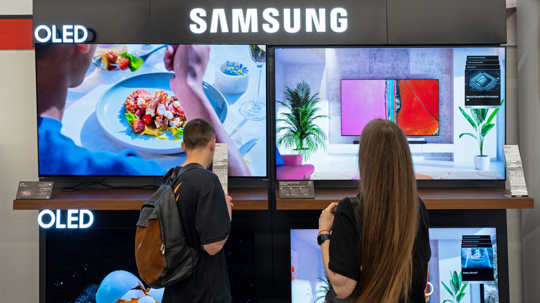 Two people looking at a display of Samsung OLED televisions in a store