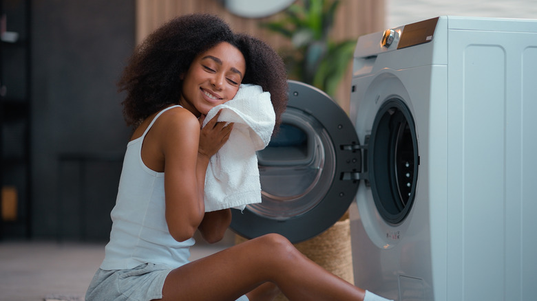 A woman feels the softness of a freshly-laundered white towel, sitting in front of her washer.