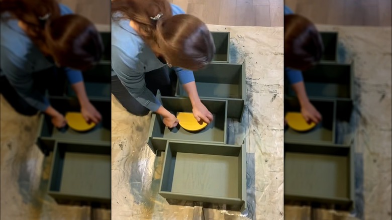 DIYer laying yellow wood embellishment in upcycled drawers fashioned as storage shelf