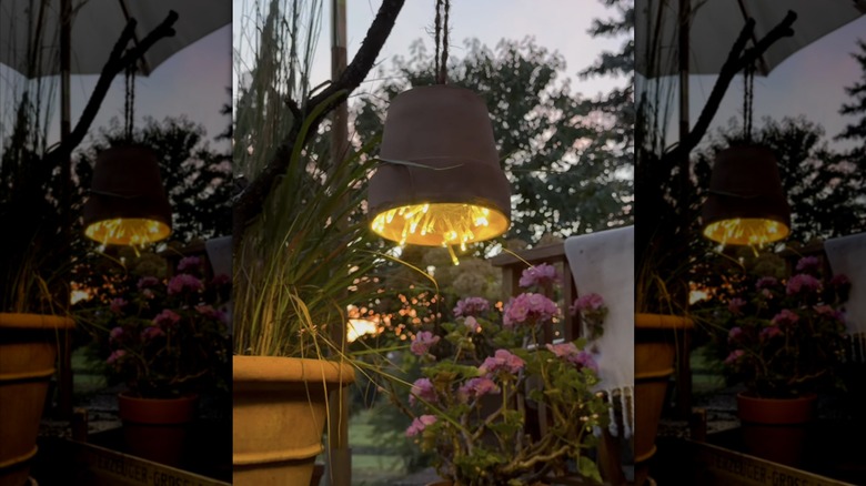 A DIY terracotta pot lantern with string lights next to pink flowers on a deck