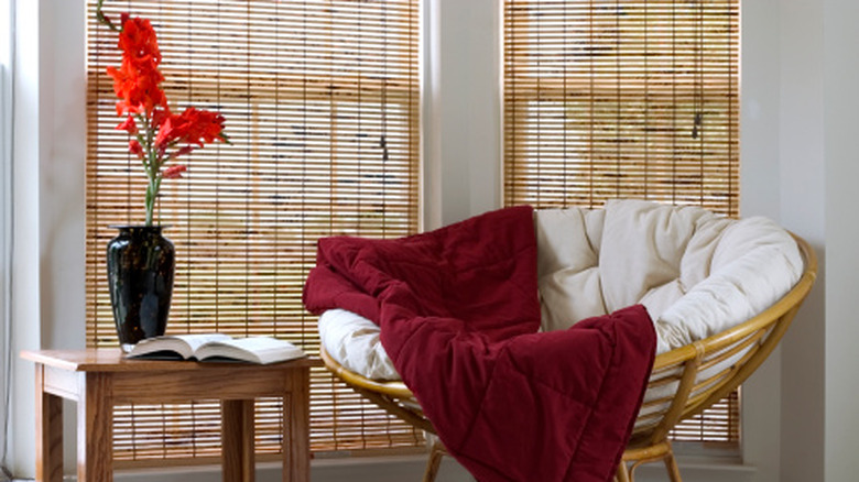 A living space with a wicker chair, a side table, and bamboo blinds in the window