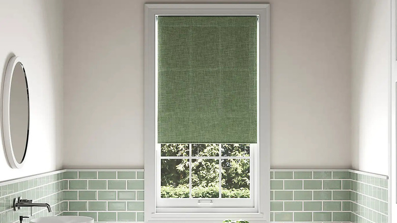 A bathroom with a green roller blind in the window