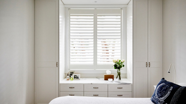 A minimalist bedroom with white plantation shutters in the window