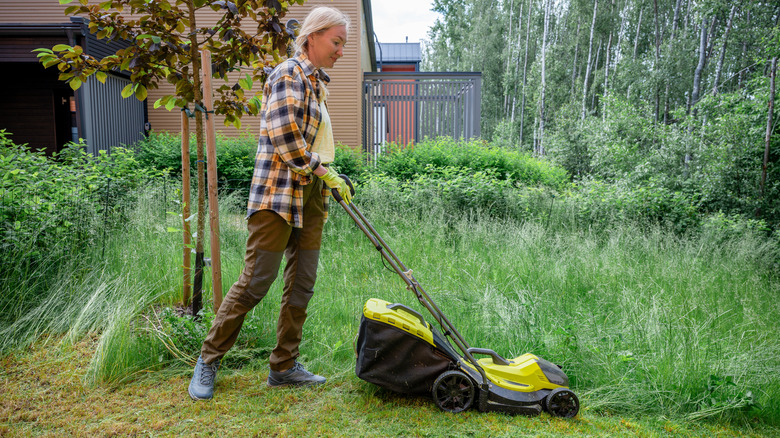 A woman uses a push mower to cut an overgrown lawn