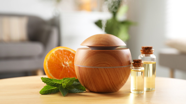 Essential oil diffuser, cosmetic products, mint and orange on wooden table at home