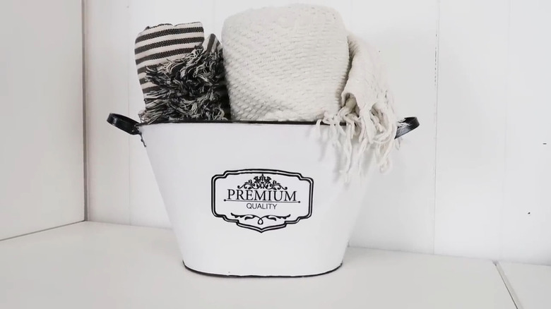 A striped and plain blanket rolled and placed in a tub painted white with a design on front