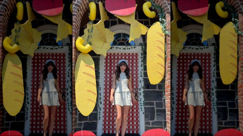 A woman stands outside a quirky front door decorated with faux baguettes and pasta