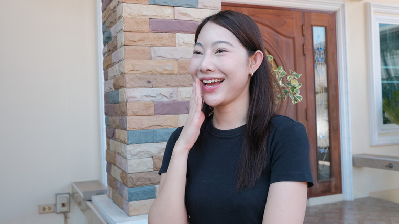 A woman smiles in shock outside a front door with a wreath