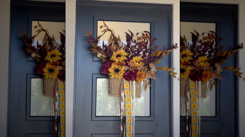 A fall-colored floral arrangement on a blue front door in a hanging wicker basket
