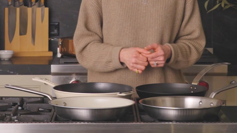Woman in beige sweater with rings standing over four frying pans on kitchen cooktop