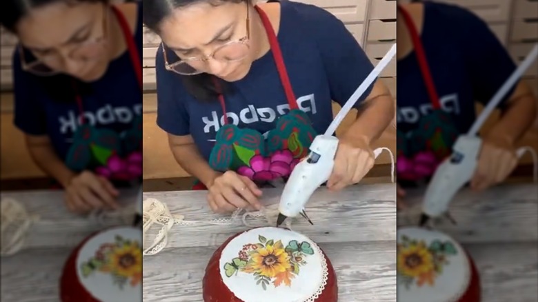 Woman hot-gluing doily flower design on back of upcycled frying pan for DIY project