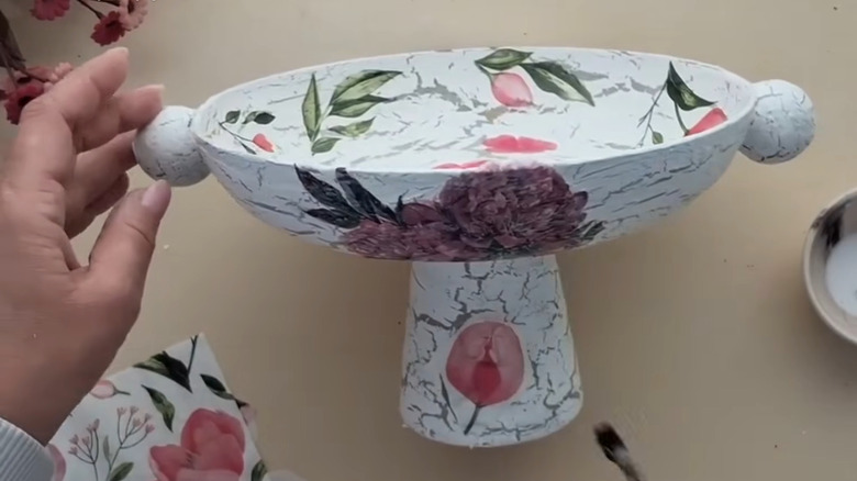 Woman decoupaging frying pan upcycle with knobs and pedestal bottom over eggshell countertop