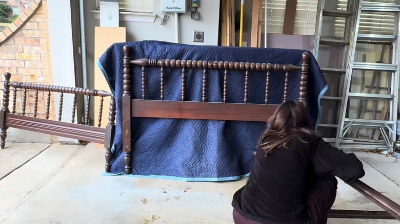 Woman preparing vintage solid wood bedframe with spindles for DIY project in home garage
