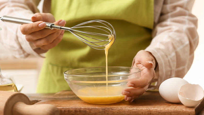 Woman using whisk to beat eggs in glass bowl