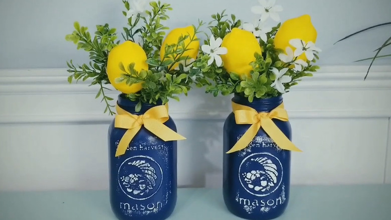 Two Mason jars painted blue with faux lemons and greenery in the top