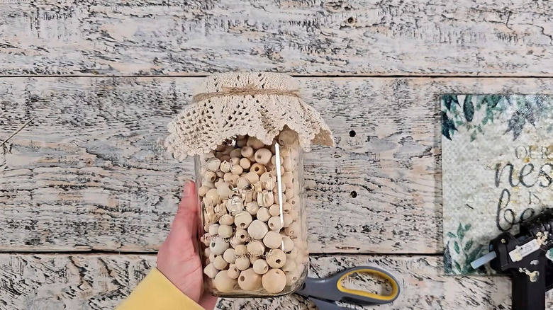 Creator holding a Mason jar full of wood beads with a doily top